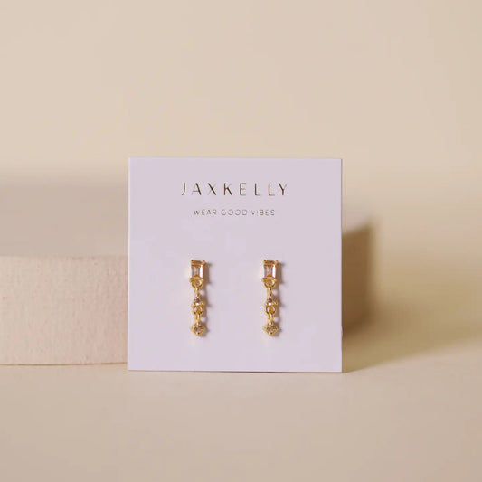 Gold earrings on a Jax Kelly branded card with a beige background