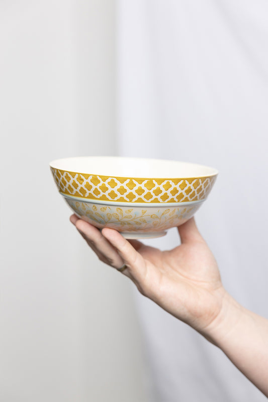 A hand holding a colorful stoneware bowl with a geometric pattern.