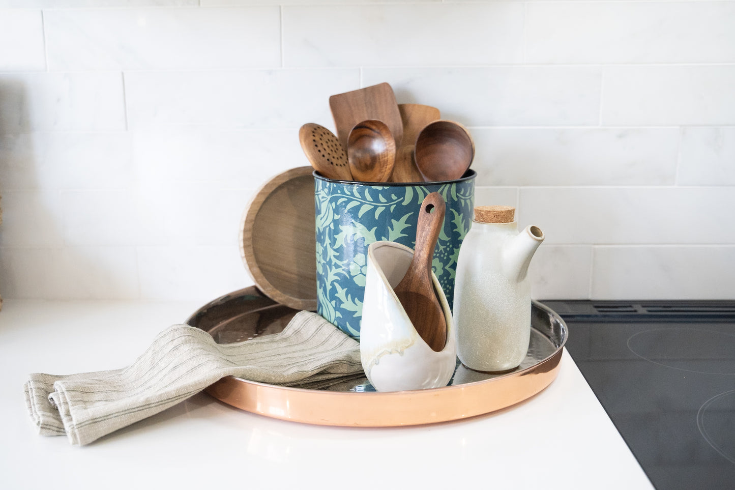 wood lid and floral designed green canister for utensil storage on counter next to oven