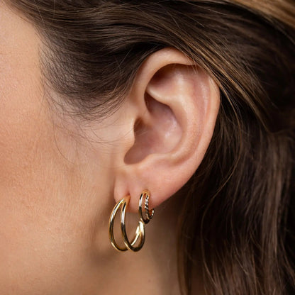 Close-up of an ear wearing gold hoop earrings with a neutral background