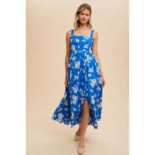 A woman wearing a blue floral cotton maxi dress with spaghetti straps, scalloped shoulder, and partially smocked back.
