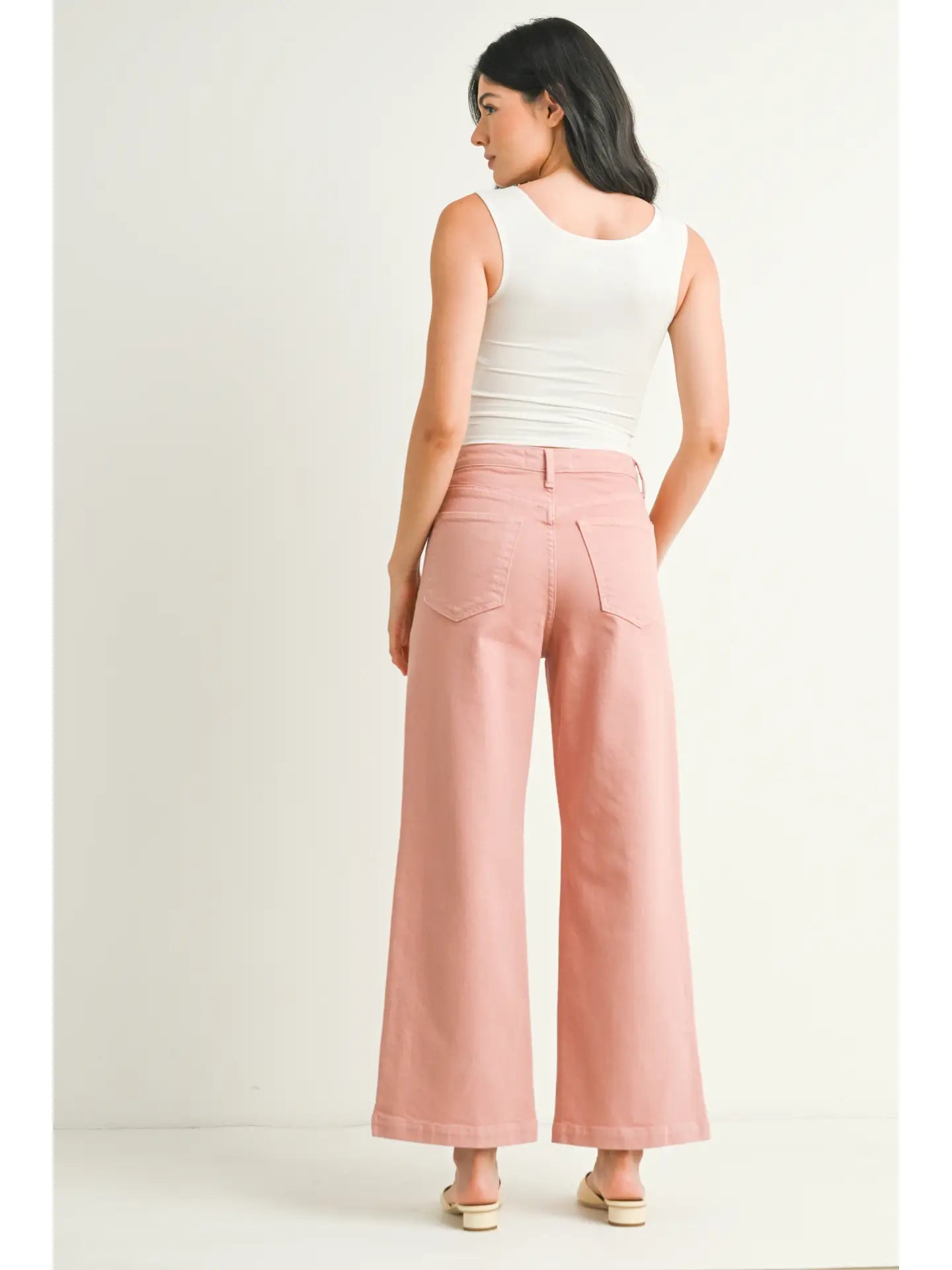 A pair of dusty coral wide leg pants with a high waist and button fly closure, displayed on a model without showing the upper part of the body.