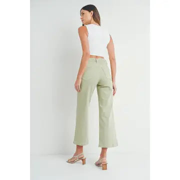 A pair of light sage wide leg pants with a high waist and button fly closure, worn by a model paired with a white top and heels.