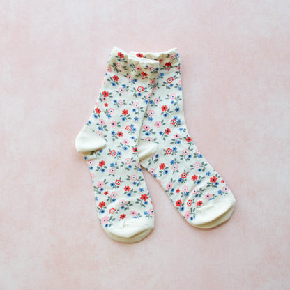 A pair of white socks with a floral pattern, displayed against a pink background.