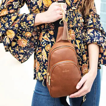 Person holding a brown leather sling bag with a floral patterned top.