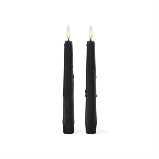Two black candles with wicks on a white background