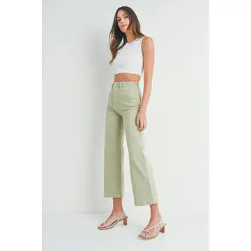 A pair of light sage wide leg pants with a high waist and button fly closure, worn by a model paired with a white top and heels.