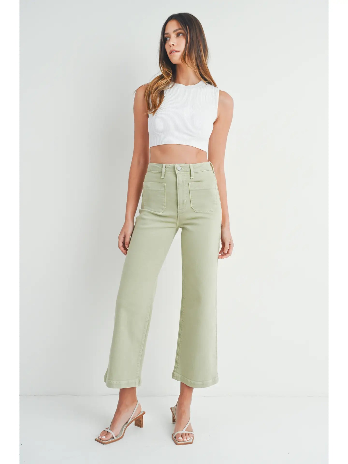 A pair of light sage wide leg pants with a high waist and button fly closure, worn by a model paired with a white top and heels.