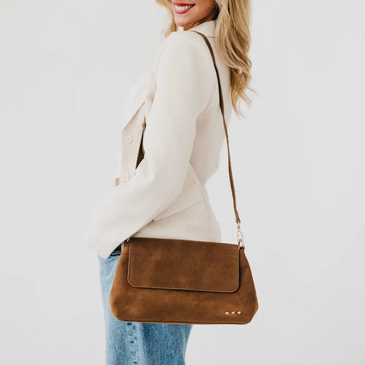 Brown suede crossbody bag with flap, snap closure, and long adjustable strap.