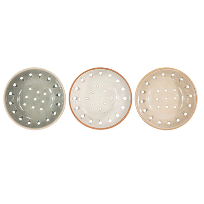 Three ceramic bowls with perforated designs in green, beige, and cream on a white background