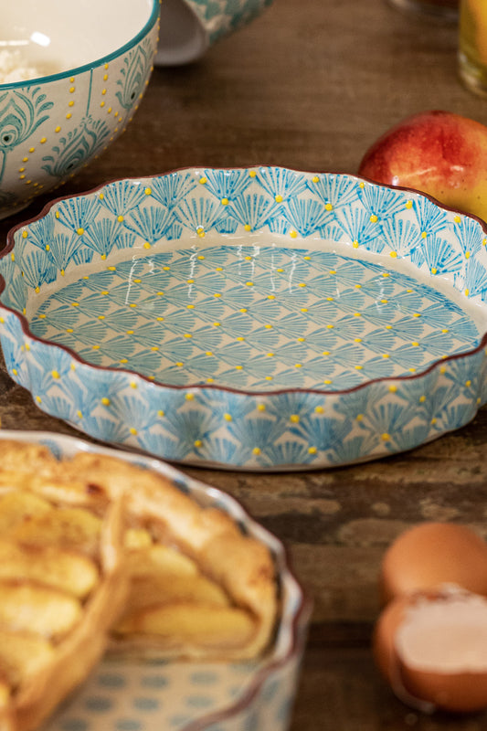 A stoneware quiche dish with a hand-stamped leaf print, displayed alongside a baked quiche and some fruits, suggesting its use in baking and serving desserts.