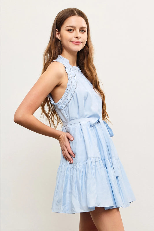 A woman wearing a sleeveless, ruffle edge blue dress with a tie at the waist.
