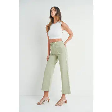 A pair of light sage wide leg pants with a high waist and button fly closure, worn by a model paired with a white top and heels.