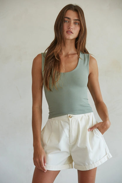 Woman wearing a green tank top and white shorts against a plain background