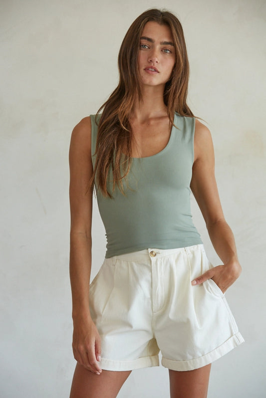 Woman wearing a green tank top and white shorts against a plain background