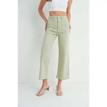 A pair of light sage wide leg pants with a high waist and button fly closure, worn by a model paired with a white top and heels.