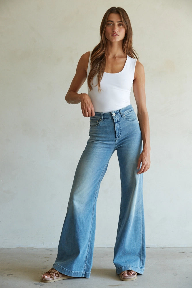 Woman wearing a white tank top and blue jeans against a plain background